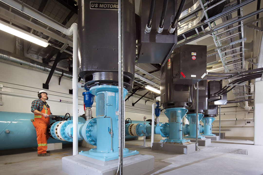 Industrial photography of a water treatment pumphouse facility interior with a worker inspecting large US Motors machinery, shot by Jason Babakaiff.