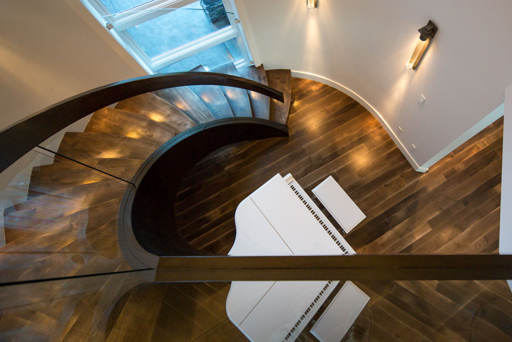 Interior architectural photography showcasing a curved wood staircase and grand piano.